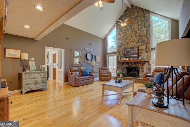 living room featuring visible vents, ceiling fan, a fireplace, beamed ceiling, and light wood-style flooring
