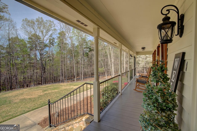 wooden deck with a yard, a porch, and a forest view