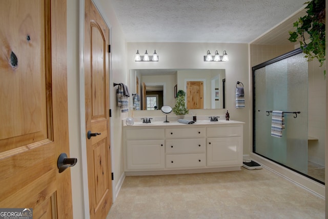 full bath featuring a sink, a textured ceiling, double vanity, and a stall shower