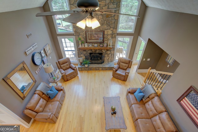 living area with a stone fireplace, a ceiling fan, a towering ceiling, and wood finished floors