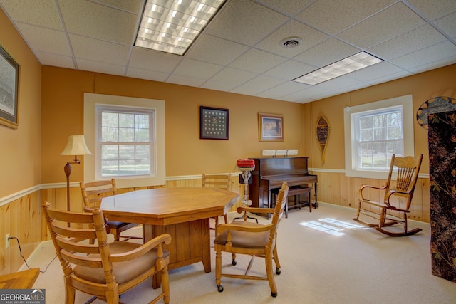 carpeted dining area with wooden walls, visible vents, a paneled ceiling, and wainscoting