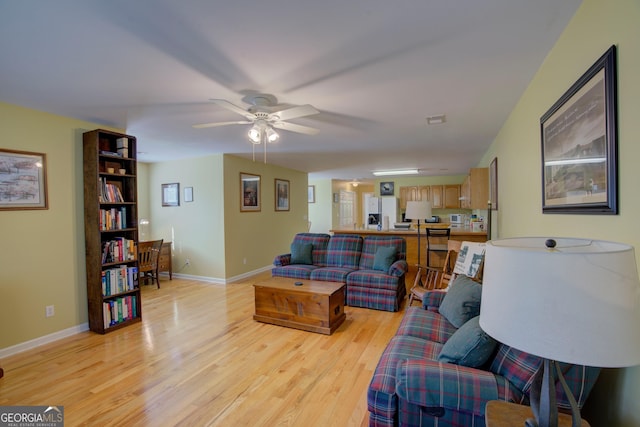 living room with ceiling fan, light wood-style floors, and baseboards