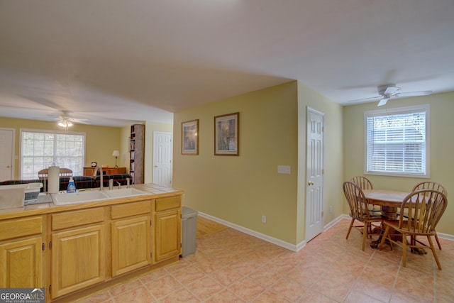 kitchen with ceiling fan, light tile patterned floors, a sink, tile counters, and baseboards