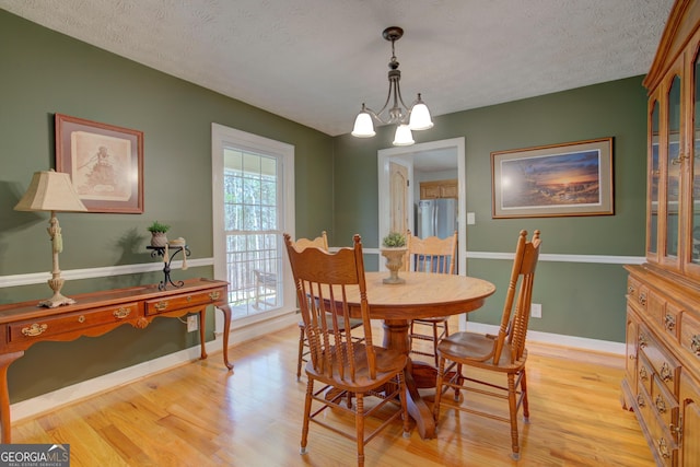 dining room featuring light wood-style floors, baseboards, a notable chandelier, and a textured ceiling