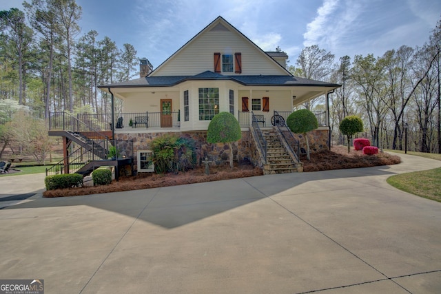 view of front of property featuring a chimney, stairway, driveway, stone siding, and a porch
