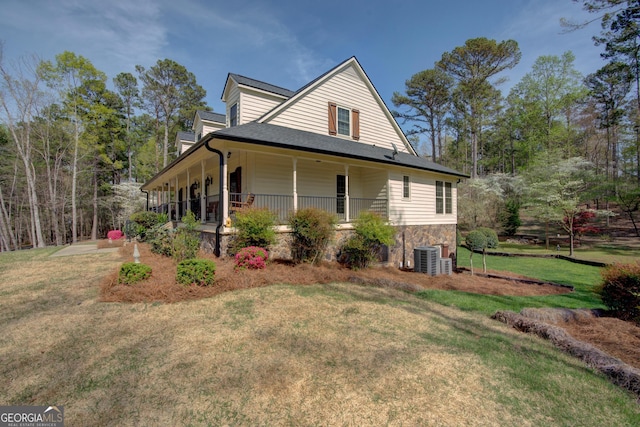 view of side of property featuring central AC unit, stone siding, covered porch, and a lawn