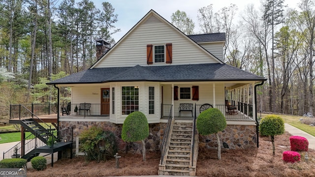 country-style home featuring stairway, roof with shingles, stone siding, and covered porch