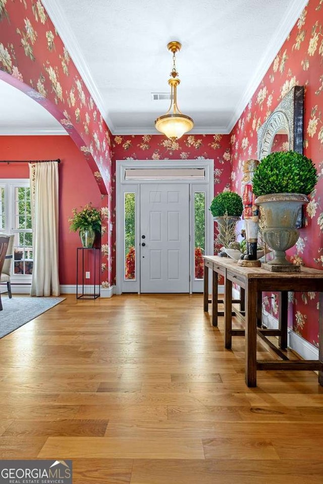 foyer featuring light wood-style flooring, arched walkways, wallpapered walls, and ornamental molding
