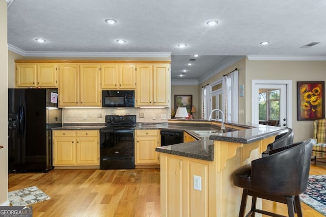 kitchen featuring a sink, black appliances, light brown cabinets, and light wood finished floors