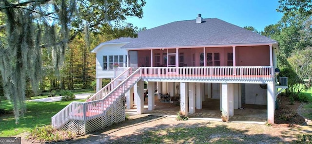 back of property with a chimney, stairway, a patio area, a sunroom, and a shingled roof
