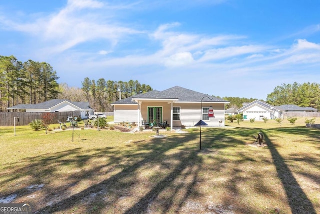 back of property with fence, a shingled roof, and a lawn