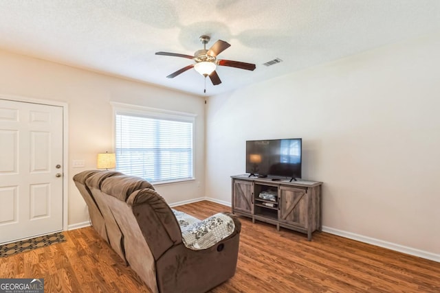 living area featuring visible vents, baseboards, a ceiling fan, a textured ceiling, and wood finished floors
