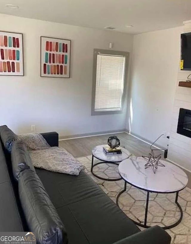 living area featuring a tiled fireplace, baseboards, and wood finished floors