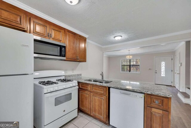 kitchen with ornamental molding, white appliances, a peninsula, brown cabinetry, and a sink