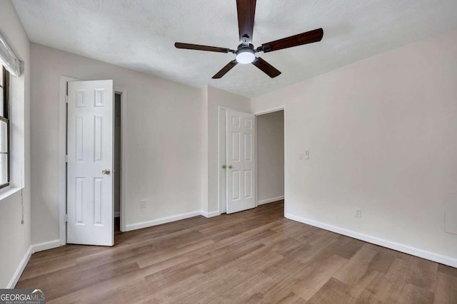 unfurnished bedroom with a textured ceiling, wood finished floors, baseboards, and multiple windows