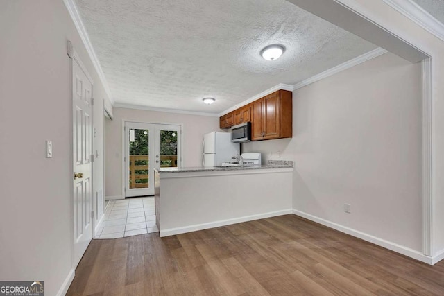 kitchen featuring ornamental molding, freestanding refrigerator, brown cabinets, stainless steel microwave, and wood finished floors