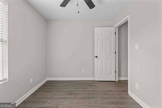 empty room featuring a textured ceiling, baseboards, a ceiling fan, and dark wood-style floors