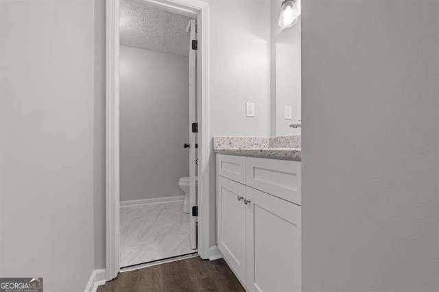 bathroom with toilet, a textured ceiling, vanity, and baseboards