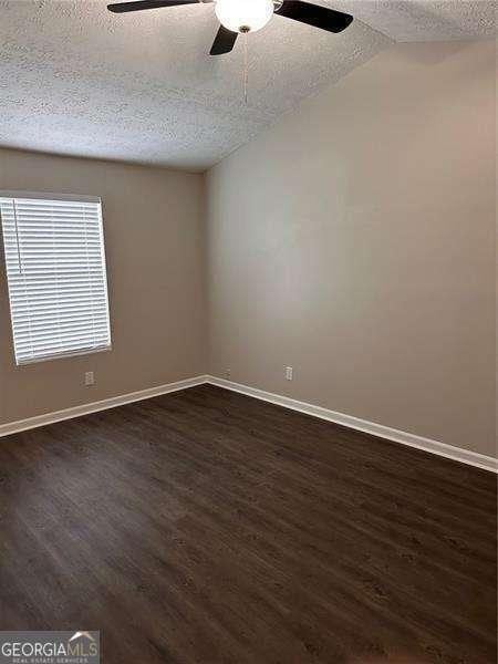unfurnished room featuring a textured ceiling, dark wood finished floors, a ceiling fan, and lofted ceiling
