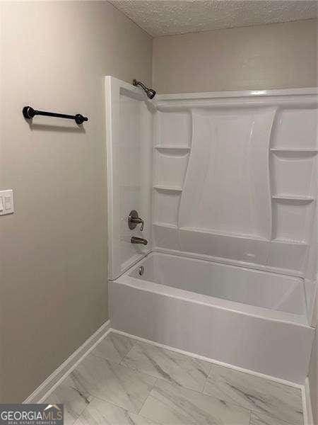 bathroom with a textured ceiling, marble finish floor, baseboards, and shower / washtub combination