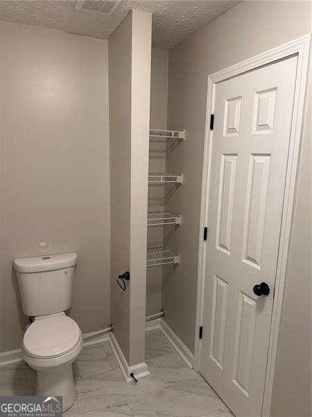 bathroom with marble finish floor, a textured ceiling, baseboards, and toilet