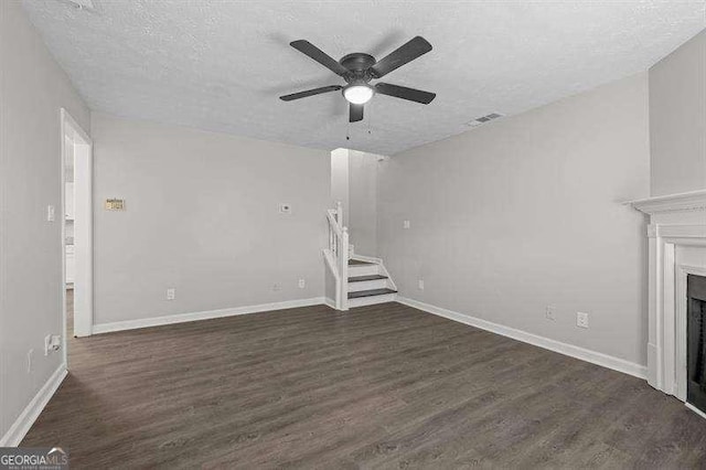 unfurnished living room with a fireplace, dark wood-style floors, a ceiling fan, and stairs