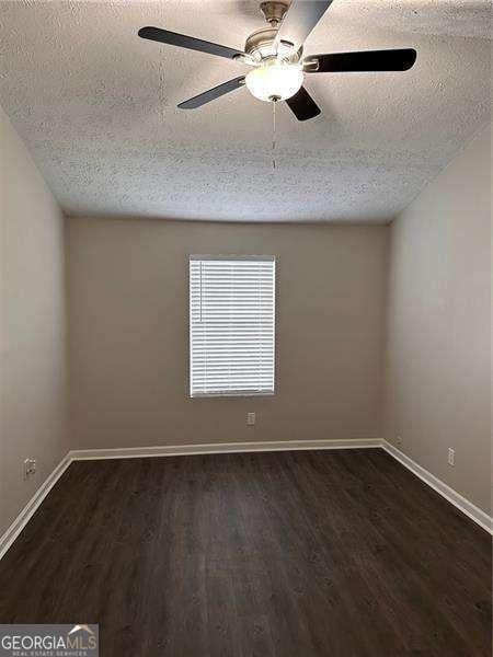 unfurnished room with dark wood-type flooring, a textured ceiling, ceiling fan, and baseboards