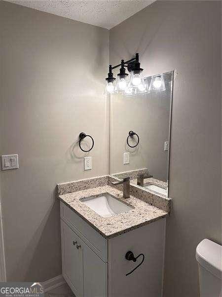 half bath featuring toilet, vanity, baseboards, and a textured ceiling