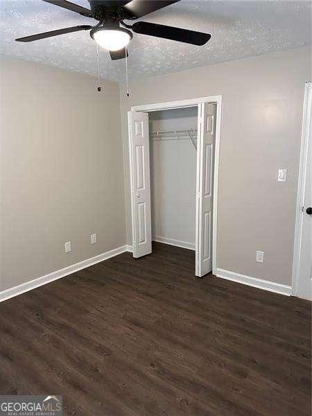 unfurnished bedroom featuring dark wood-style flooring, a closet, baseboards, and a textured ceiling
