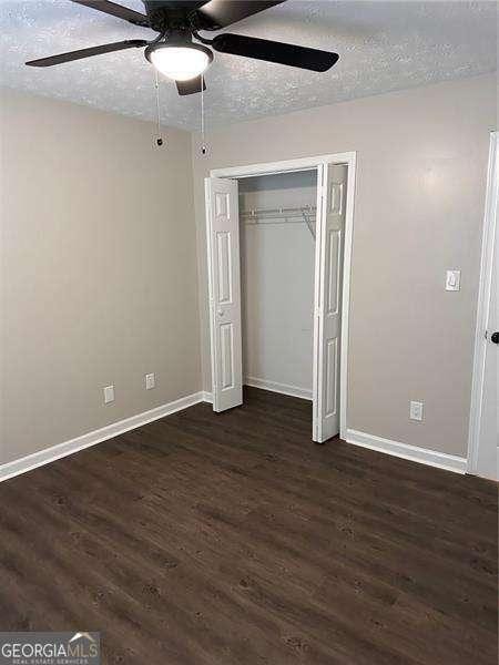 unfurnished bedroom featuring a closet, dark wood-style flooring, a textured ceiling, and baseboards