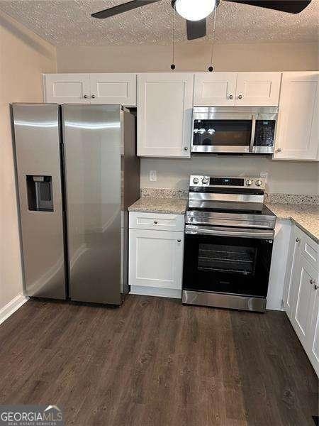 kitchen featuring dark wood-style flooring, white cabinetry, a textured ceiling, and appliances with stainless steel finishes