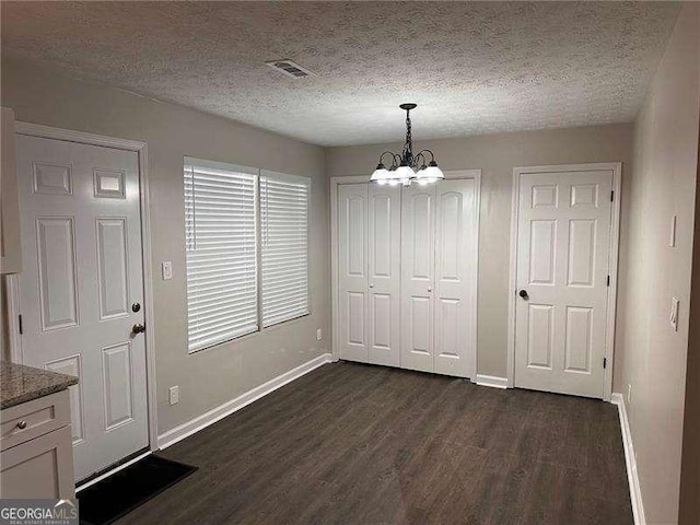 unfurnished dining area with a textured ceiling, baseboards, an inviting chandelier, and dark wood finished floors