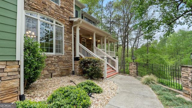 view of exterior entry with a ceiling fan, fence, and stone siding