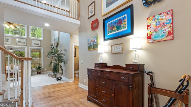 corridor featuring light wood-style floors, a towering ceiling, baseboards, and stairway