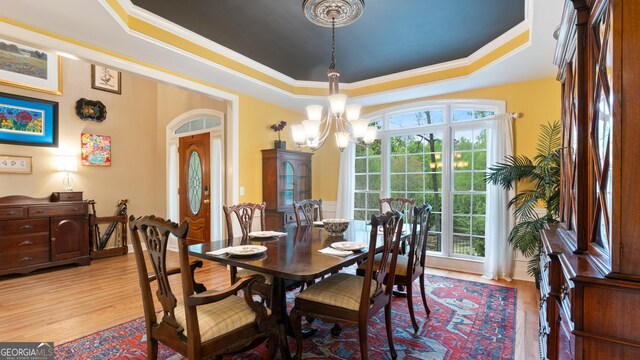 dining room featuring crown molding, a tray ceiling, light wood finished floors, and a notable chandelier