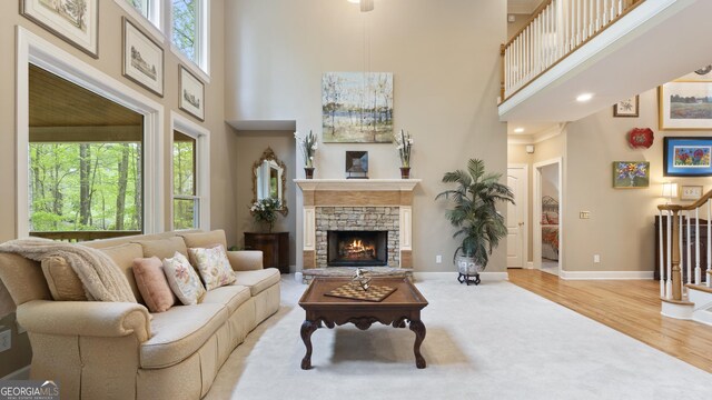 living area with baseboards, a stone fireplace, recessed lighting, wood finished floors, and a towering ceiling
