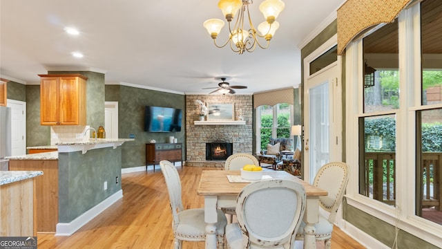 dining space with baseboards, ornamental molding, light wood-style floors, a fireplace, and ceiling fan with notable chandelier
