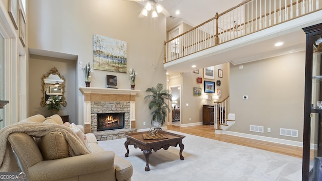 living area with visible vents, a stone fireplace, ceiling fan, a towering ceiling, and stairs