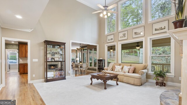 living area featuring ornamental molding, a ceiling fan, a towering ceiling, and a fireplace