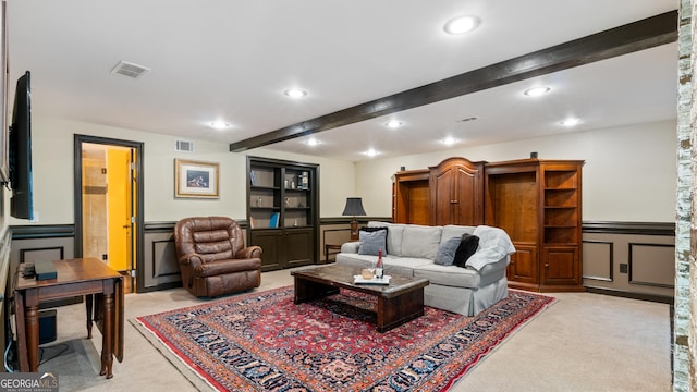 living room featuring a decorative wall, beamed ceiling, visible vents, a wainscoted wall, and light carpet