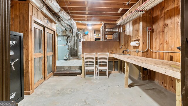 unfinished below grade area featuring wooden walls, gas water heater, heating unit, and a sink