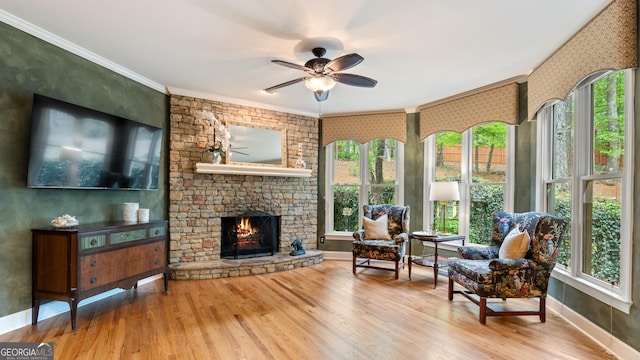 interior space featuring wood finished floors, a stone fireplace, ornamental molding, and ceiling fan