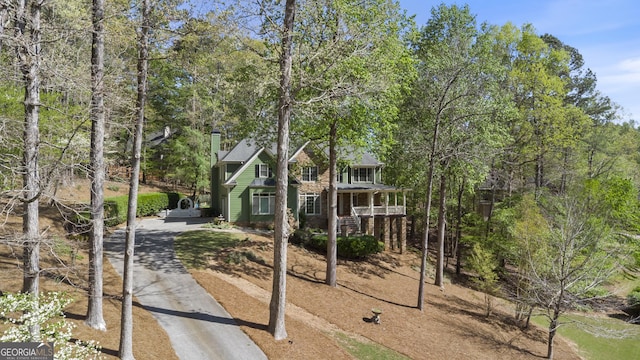 view of front of house featuring aphalt driveway, a chimney, and covered porch
