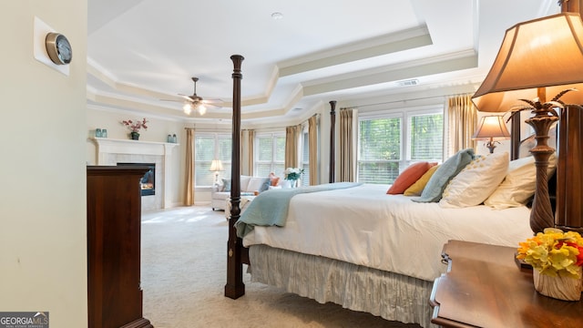 carpeted bedroom with crown molding, a fireplace, a tray ceiling, a ceiling fan, and visible vents