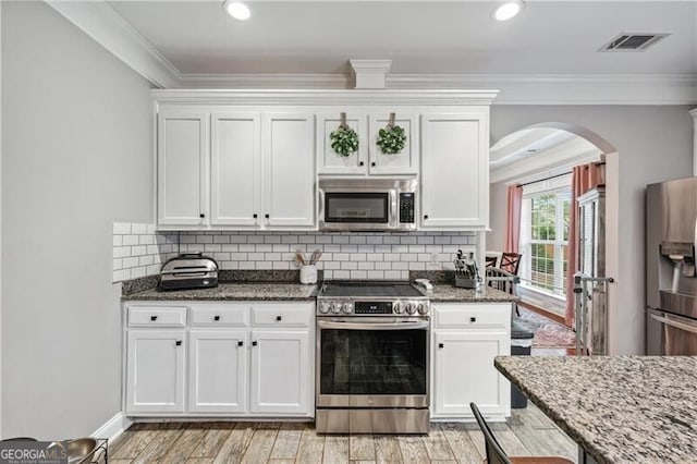 698 Jefferson Hwy, Winder, GA 30680 - kitchen with stainless steel appliances, arched walkways, white cabinetry, dark stone countertops, and crown molding