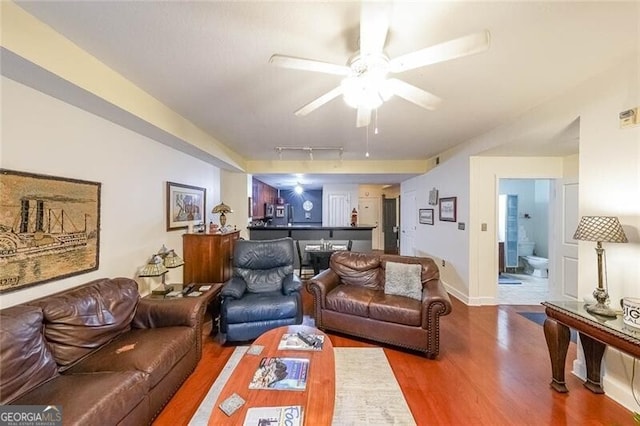 living room featuring track lighting, ceiling fan, baseboards, and wood finished floors