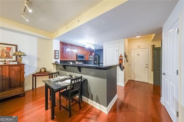 kitchen featuring dark countertops, a peninsula, dark wood finished floors, stainless steel microwave, and refrigerator