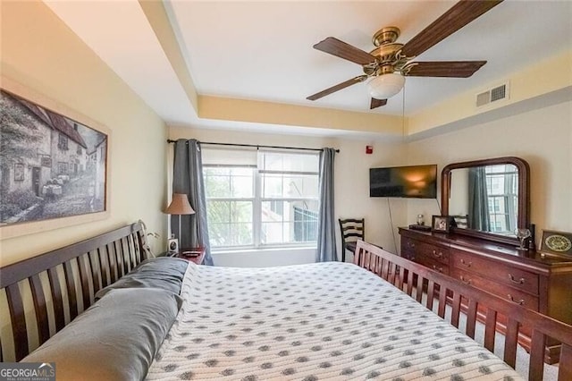 bedroom featuring visible vents, a raised ceiling, and a ceiling fan