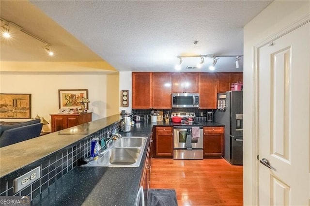 kitchen featuring light wood-style flooring, dark countertops, a sink, stainless steel appliances, and backsplash