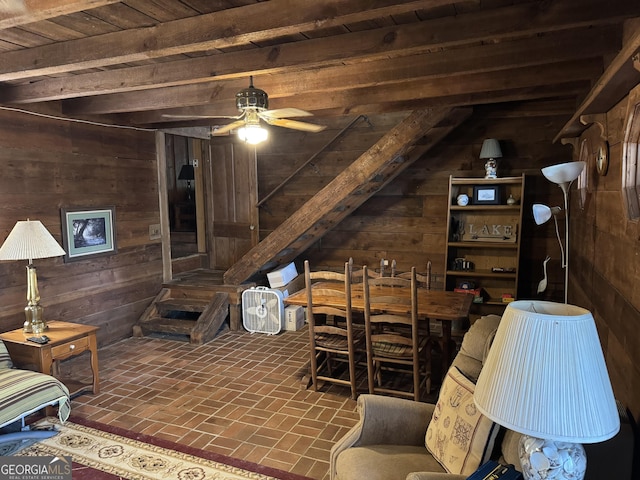 living room with a ceiling fan, wood ceiling, wooden walls, beamed ceiling, and brick floor